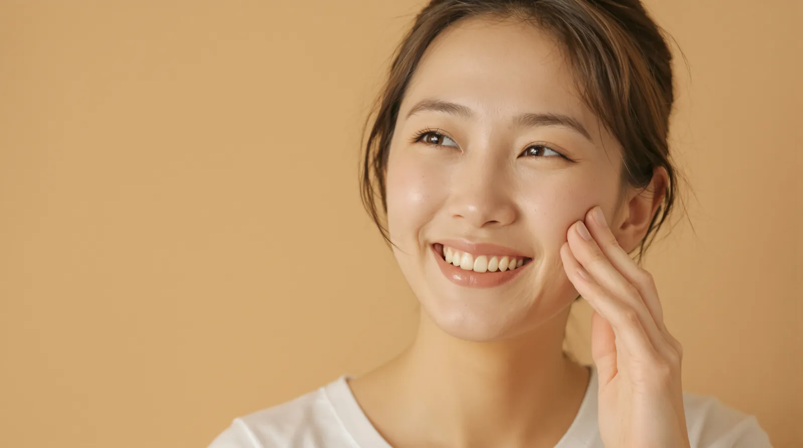 A smiling woman gently touches her cheek