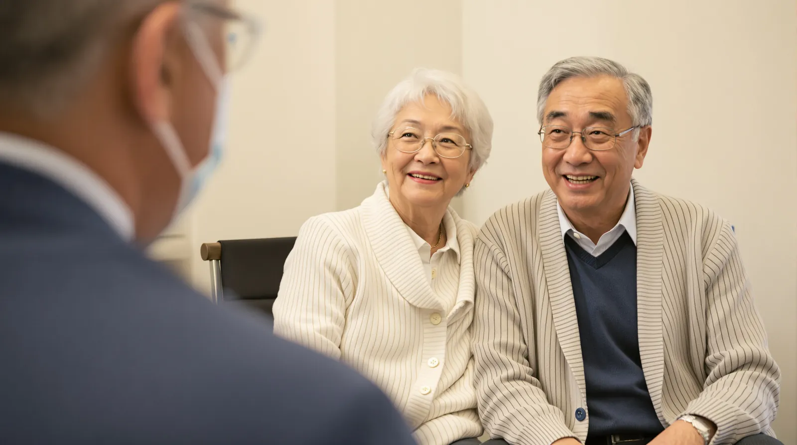 An older couple in cardigans sit together and smile during a doctor's visit