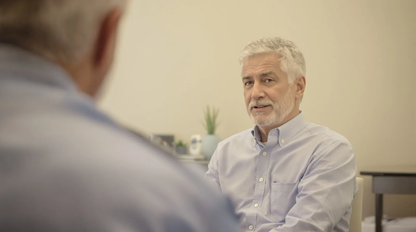 A man with grey hair listens during a consultation in a bright office